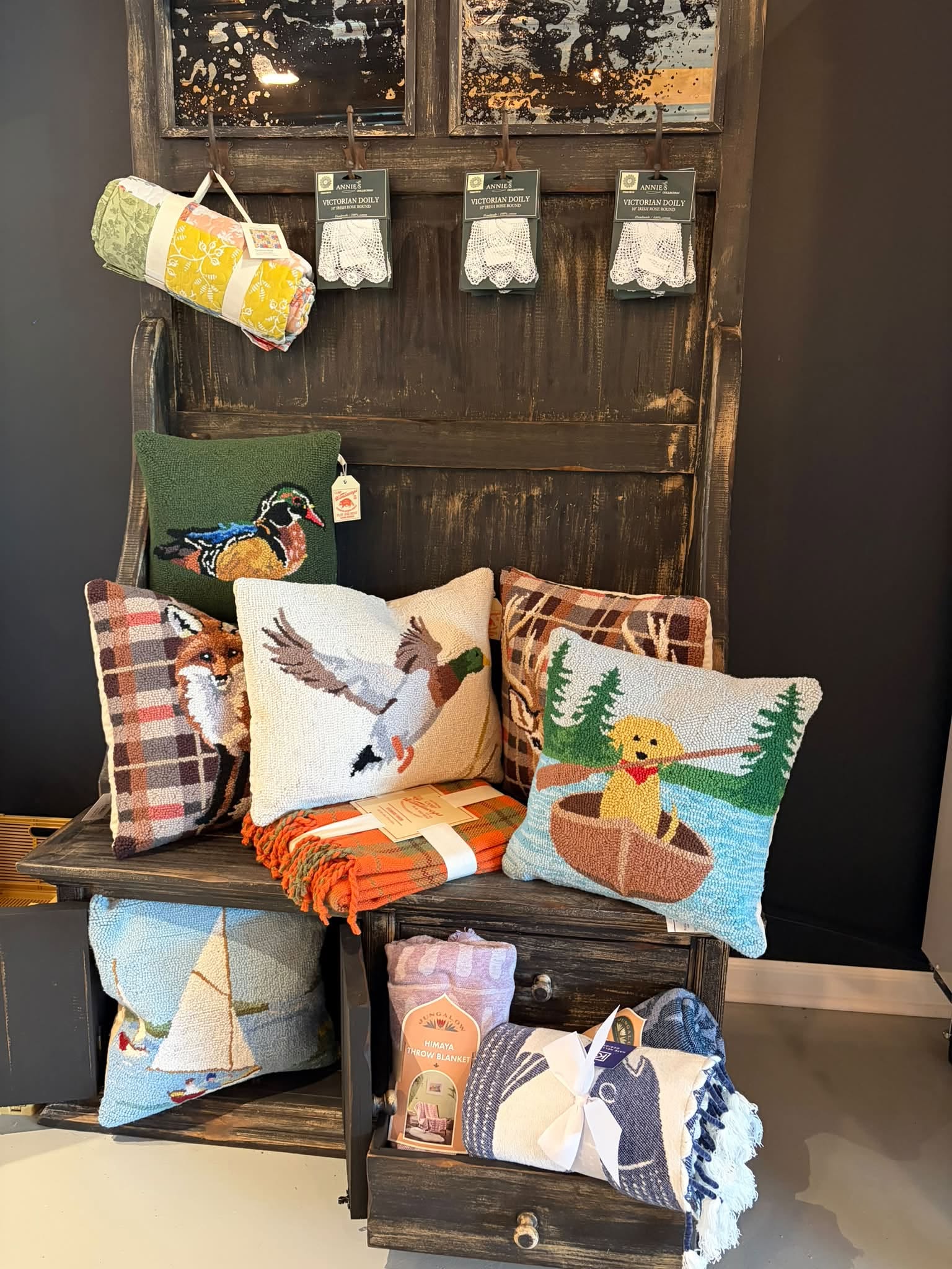 A rustic display of hand-hooked pillows, plaid throws, and lace doilies at Bennington Farms